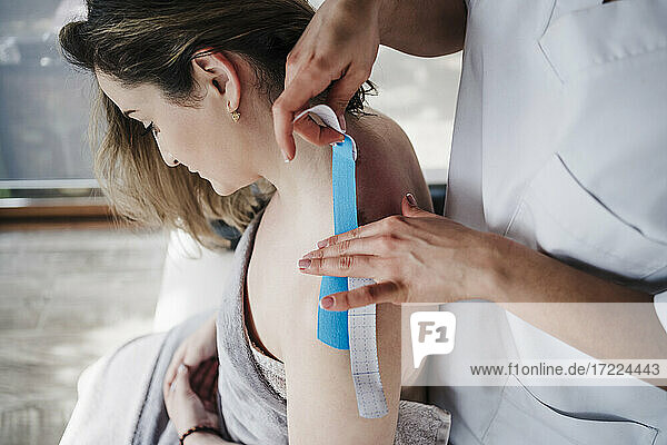 Therapeutin klebt elastisches therapeutisches Band auf die Schulter eines Patienten im Krankenhaus