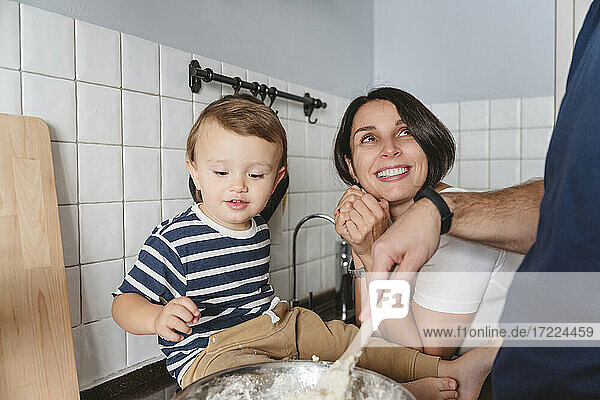 Aufgeregte Mutter mit Sohn  die ihrem Mann bei der Zubereitung von Speisen in der Küche zusieht