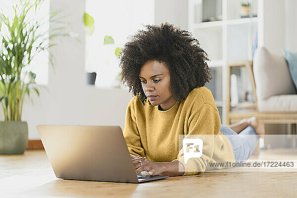 Frau benutzt Laptop  während sie zu Hause auf dem Boden liegt