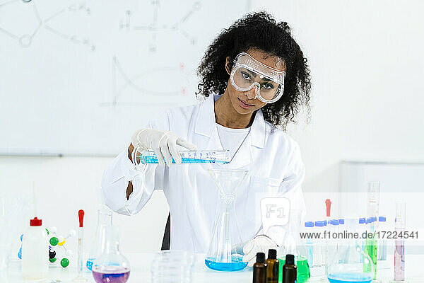 Eine Forscherin gießt eine Flüssigkeit in einen Kolben  während sie in einem Labor experimentiert