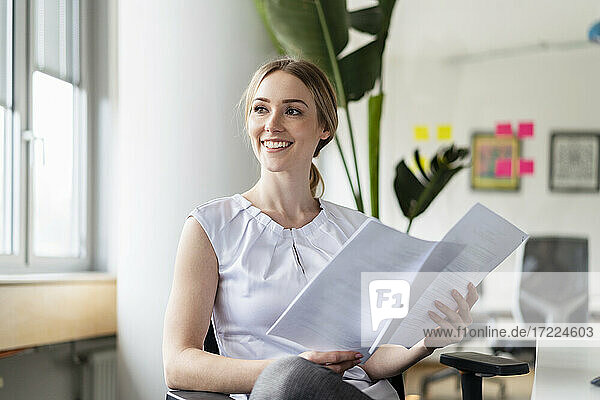 Contemplating businesswoman with documents smiling while looking away in office