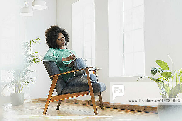 Frau  die mit einem Buch auf einem Sessel zu Hause sitzt und träumt