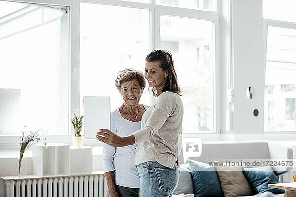 Happy woman with grandmother taking selfie through digital tablet at home