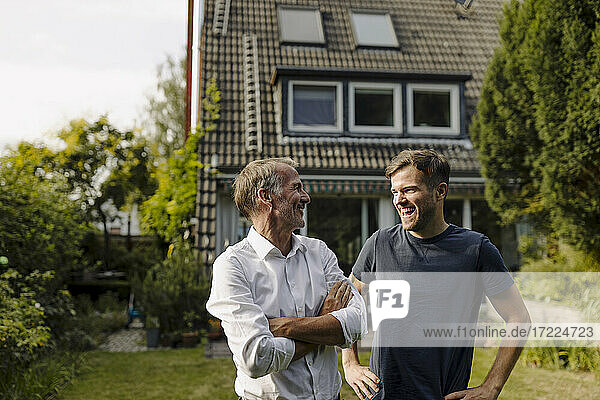 Lächelnder Vater mit verschränkten Armen  der seinen fröhlichen Sohn anschaut  während er im Hinterhof steht
