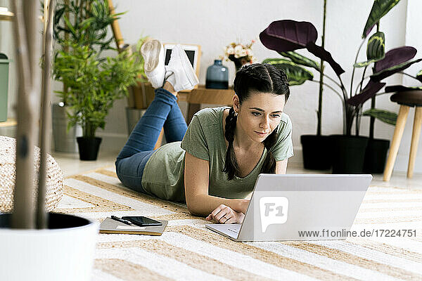Schöne Frau  die einen Laptop benutzt  während sie zu Hause auf dem Teppich liegt