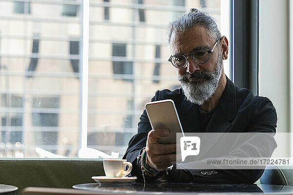 Geschäftsmann mit Brille benutzt Smartphone in einem Café