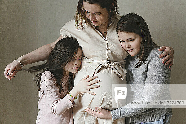 Töchter umarmen schwangere Mutter  die zu Hause steht
