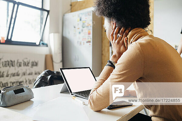Junge afrikanische Frau benutzt einen Laptop  während sie an einem Tisch im Studio sitzt