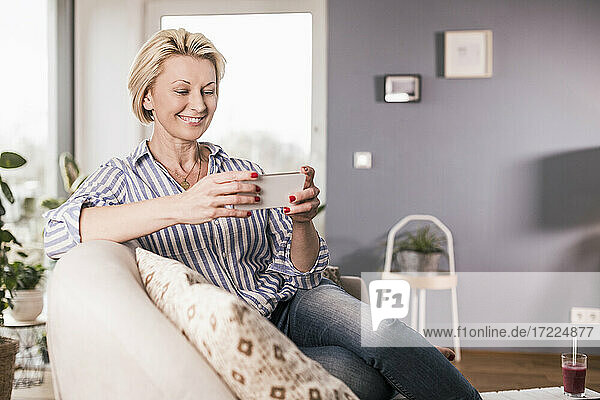 Reife Frau schaut auf Smartphone im Wohnzimmer