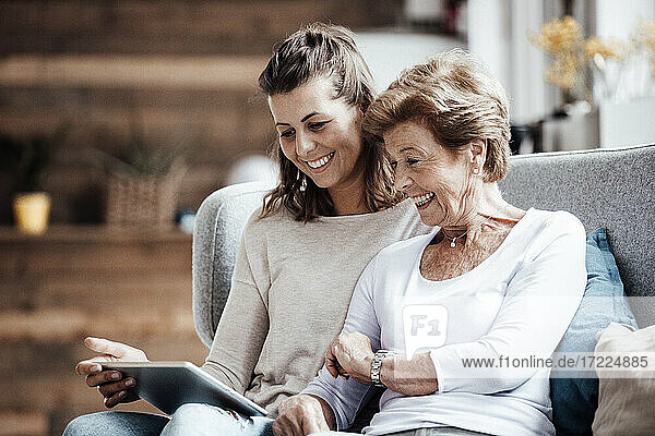 Glückliche Großmutter und Frau schauen auf ein digitales Tablet  während sie zu Hause auf dem Sofa sitzen