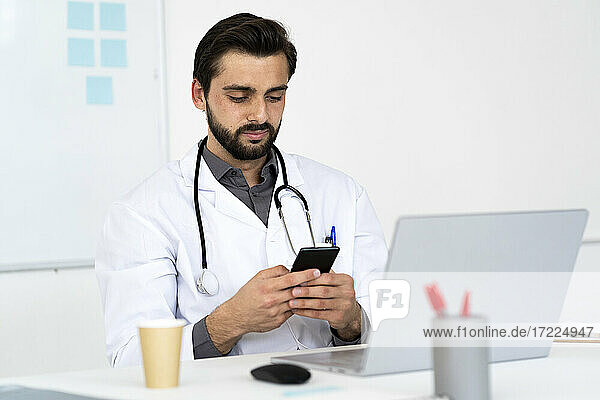 Male doctor using mobile phone while sitting at desk