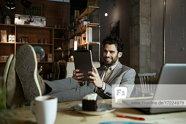 Smiling businessman on video call through digital tablet in illuminated cafe