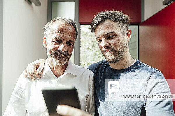 Vater und Sohn benutzen ihr Smartphone zu Hause an einem sonnigen Tag