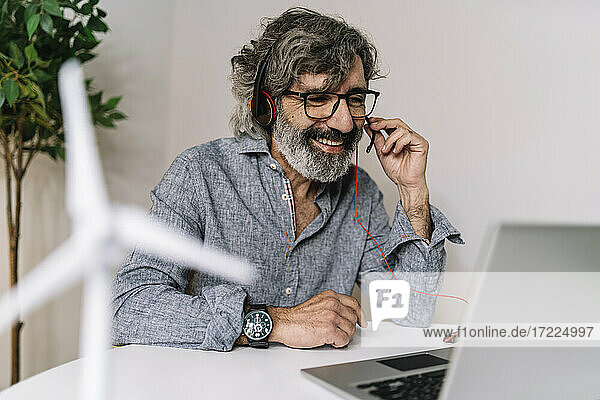 Smiling senior businessman with headset during video call on laptop at office