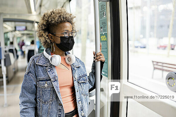Mittlere erwachsene Frau mit Gesichtsschutzmaske steht und schaut durch ein Straßenbahnfenster