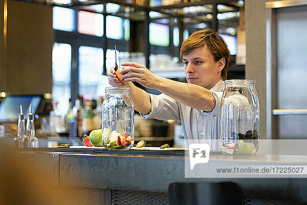 Young man adding strawberries in jar during fruit preparation at bar counter