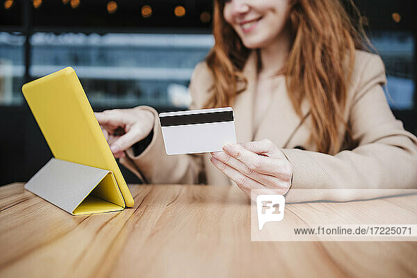 Lächelnde junge Frau  die ein digitales Tablet benutzt  während sie in einem Café mit einer Kreditkarte bezahlt