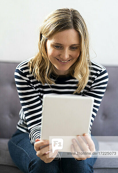 Mittlere erwachsene Frau lächelt  während sie ein digitales Tablet zu Hause benutzt