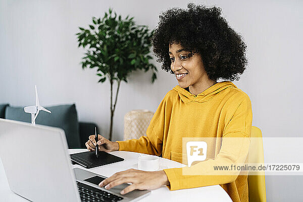 Frau mit Grafiktablett und Laptop  zu Hause sitzend