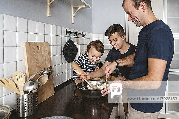 Fröhliche Söhne helfen ihrem Vater bei der Zubereitung von Speisen in der Küche zu Hause
