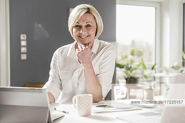 Smiling female entrepreneur with digital tablet and laptop sitting at table in home office