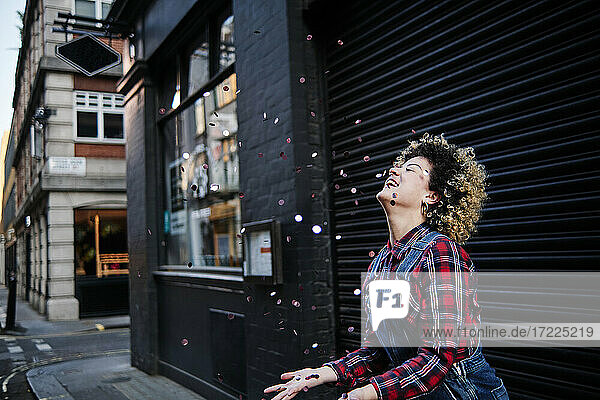 Smiling woman with eyes closed enjoying confetti falling in front of shutter