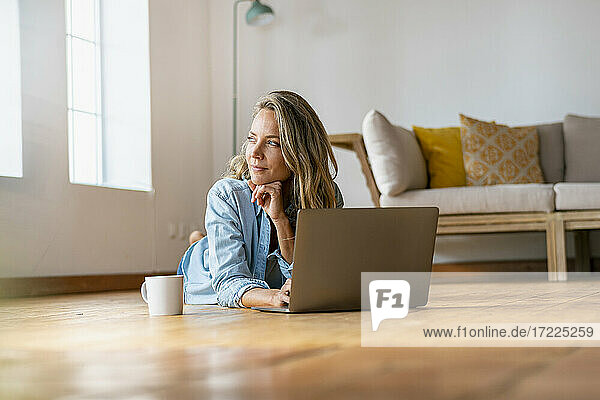 Nachdenkliche Frau  die wegschaut  während sie mit ihrem Laptop zu Hause liegt