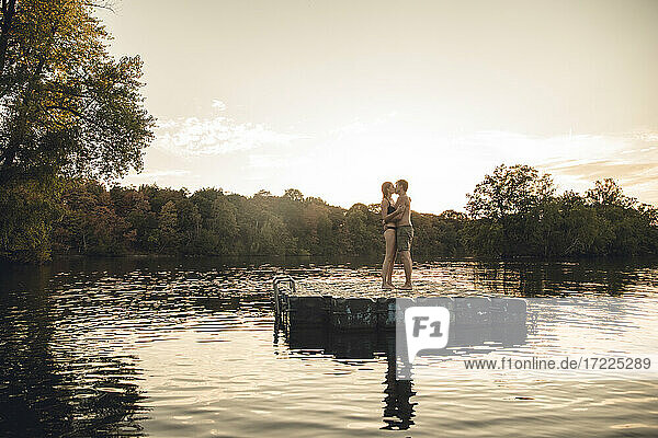 Junges Paar  das auf einer Badeplattform an einem See steht  sich umarmt und küsst