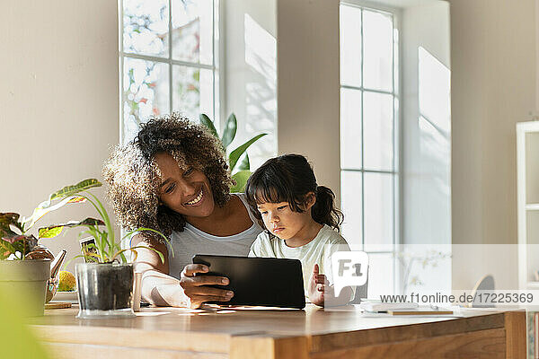 Lächelnde Mutter und Tochter schauen auf ein digitales Tablet  während sie im Wohnzimmer sitzen
