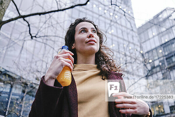 Contemplating woman holding bottle of juice while looking away