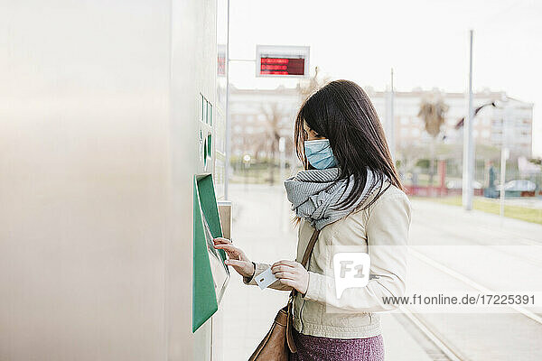 Woman with protective face mask buying ticket at kiosk during COVID-19