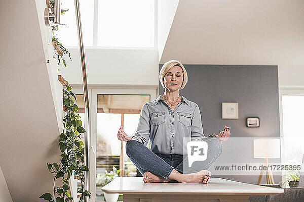 Woman sitting in lotus position on table at home