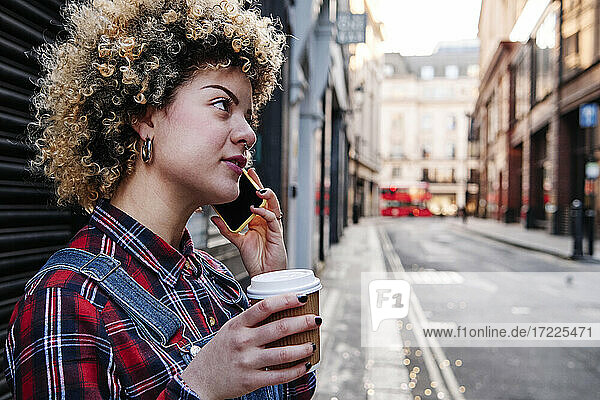 Curly haired woman having coffee while talking on smart phone