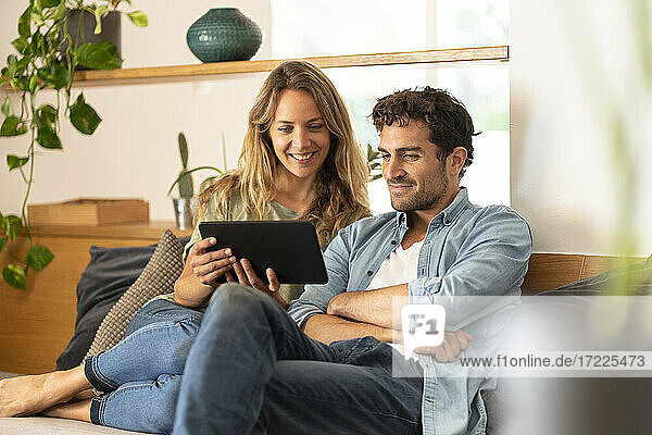 Lächelnde Frau mit Freund  die zu Hause auf ein digitales Tablet schaut