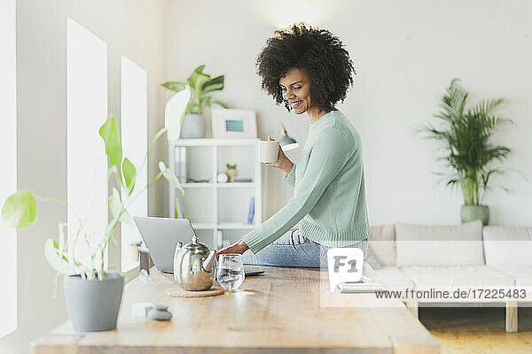 Smiling woman with coffee cup using laptop on table at home