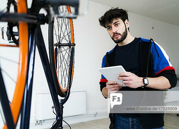 Mann schaut auf ein umgestürztes Fahrrad  während er zu Hause ein digitales Tablet hält