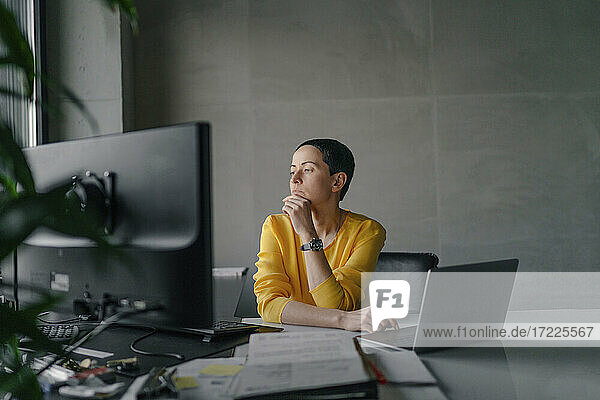 Nachdenkliche Geschäftsfrau  die am Schreibtisch im Büro sitzt und wegschaut