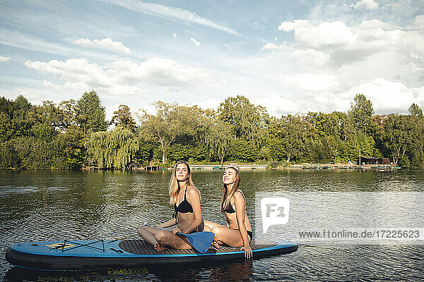 Freundinnen nehmen ein Sonnenbad auf einem Paddelbrett auf dem See