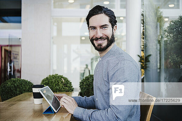 Lächelnder Geschäftsmann mit digitalem Tablet auf dem Schreibtisch am Arbeitsplatz