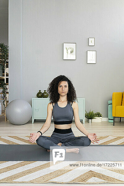 Young woman practicing lotus position on exercise mat in living room