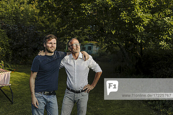 Son with father looking away while standing in back yard