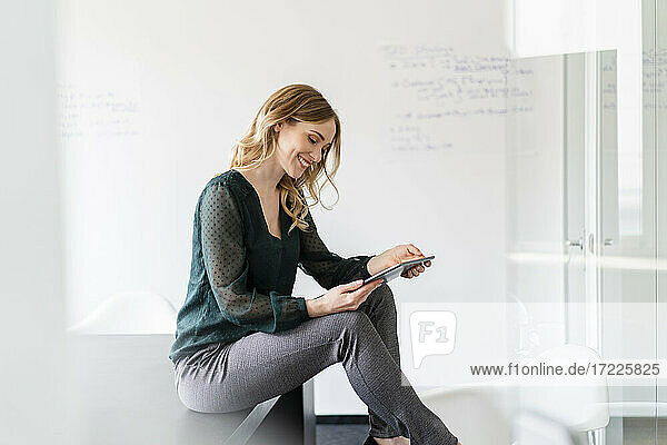 Zufriedene Geschäftsfrau  die ein digitales Tablet benutzt  während sie auf einem Konferenztisch im Büro sitzt