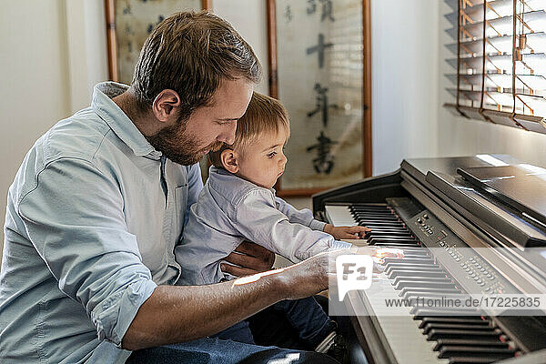 Vater gibt seinem Sohn Klavierunterricht  der zu Hause auf dem Schoß sitzt