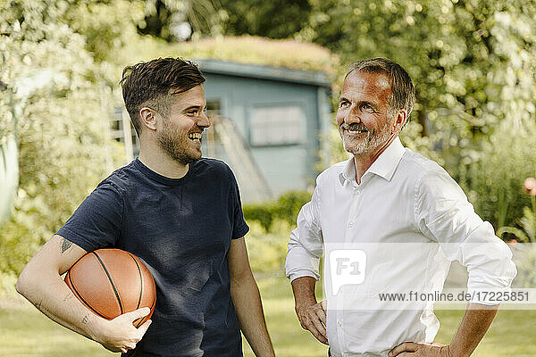 Fröhlicher Sohn mit Basketball  der seinen Vater anschaut  während er im Hinterhof steht