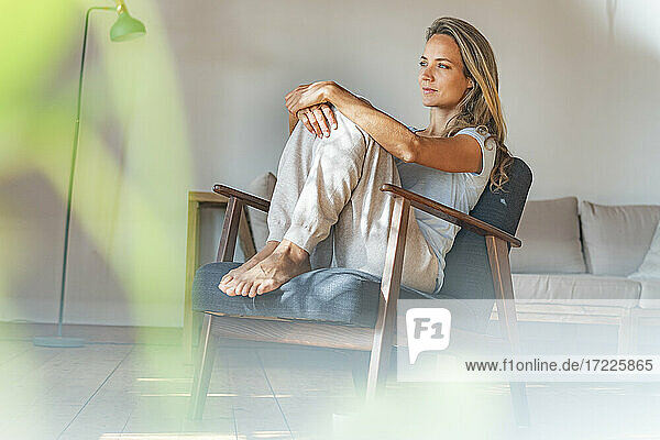 Nachdenkliche Frau schaut weg  während sie zu Hause auf einem Sessel sitzt