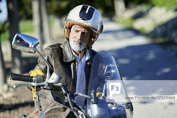 Nachdenklicher Mann mit Helm auf einem Motorrad sitzend