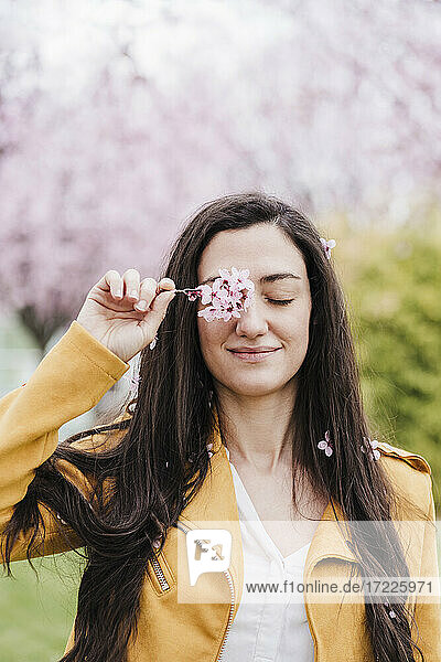 Lächelnde Frau bedeckt Auge mit Blumen im Frühling