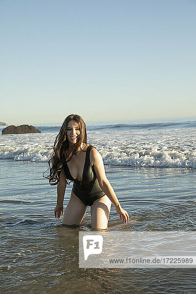 Smiling supermodel playing in water while kneeling at beach