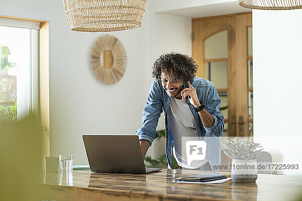 Male entrepreneur using laptop while talking on phone at home