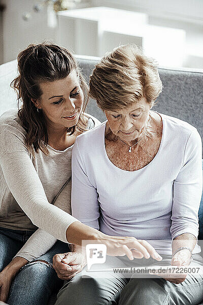 Junge Frau benutzt digitales Tablet  das von der Großmutter auf dem Sofa gehalten wird